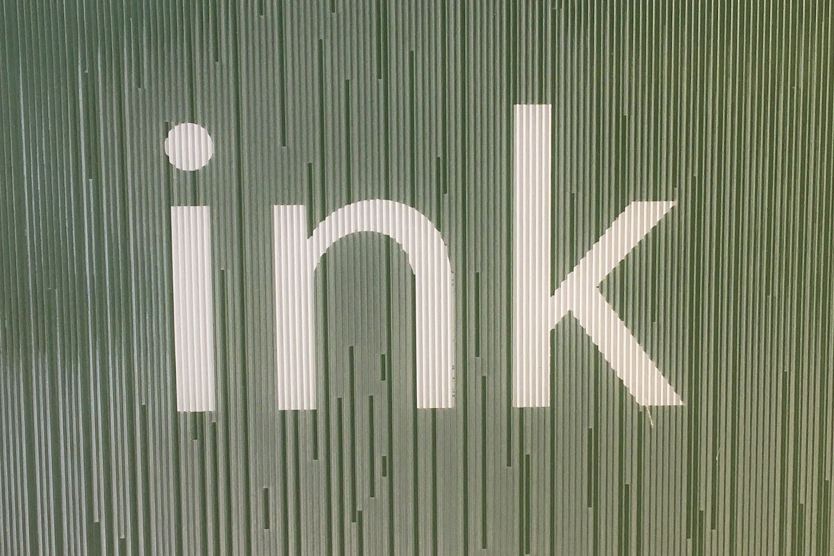 Gröna glaspaneler i linjerat mönster med vita bokstäver som formar ordet INK