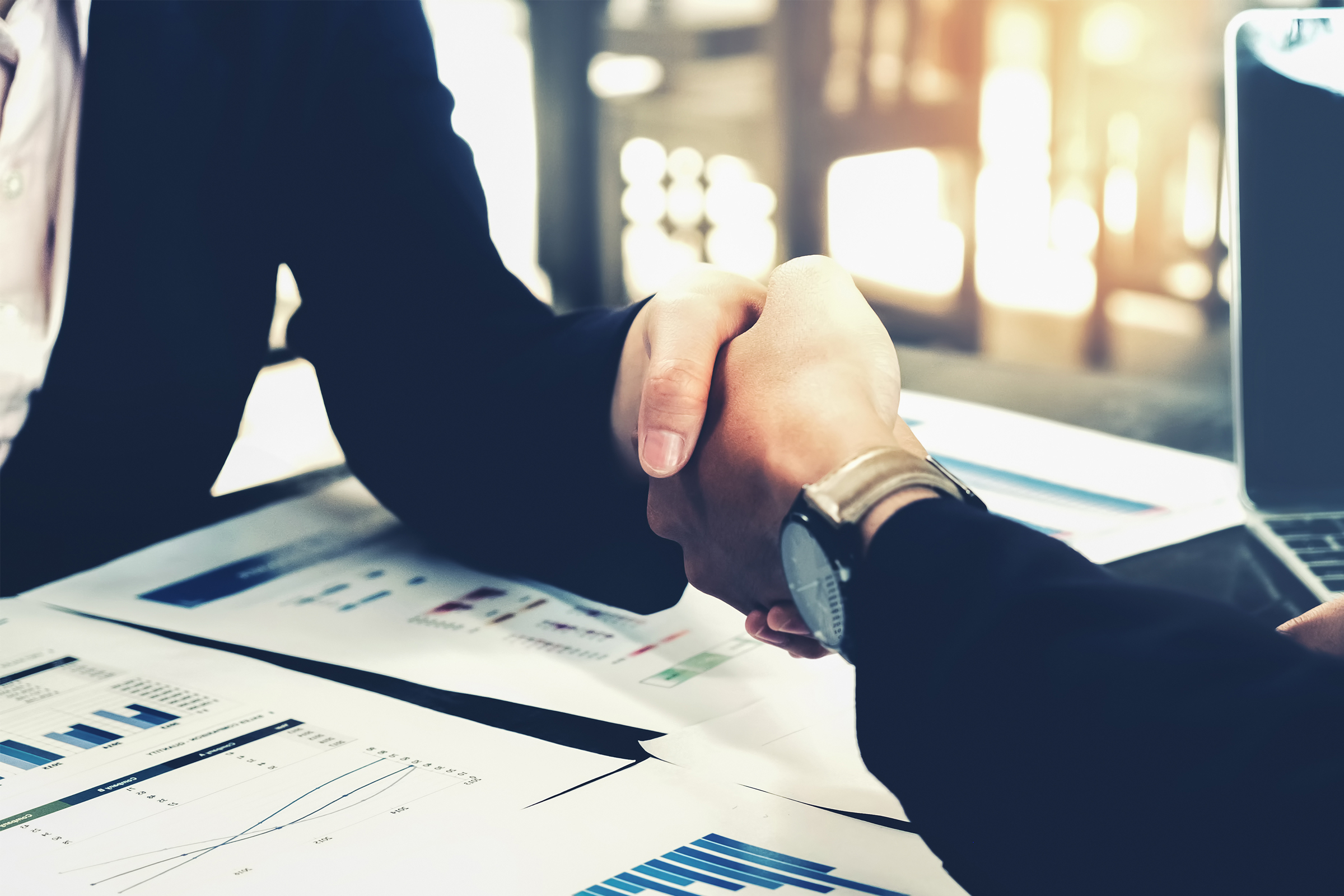 Två händer skakar hand över ett skrivbord med dokument.
